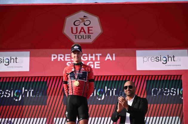 Tim Merlier wearing the red leader's jersey on the podium